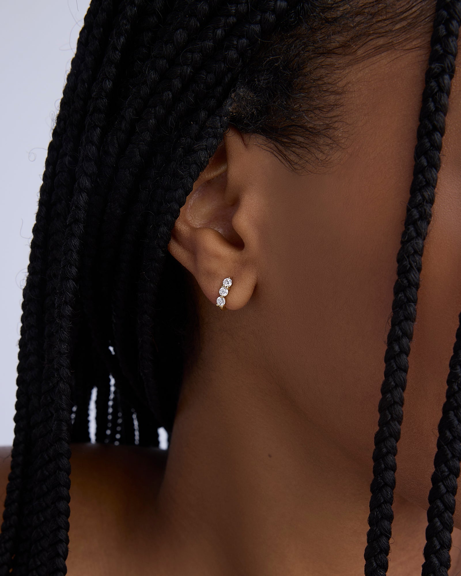 Close-up of an ear wearing a diamond earring with braided hair.