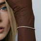 Image of model wearing tennis bracelet layered over the sleeve of a brown top. 