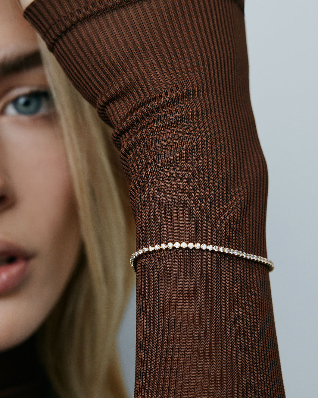 Image of model wearing tennis bracelet layered over the sleeve of a brown top. 