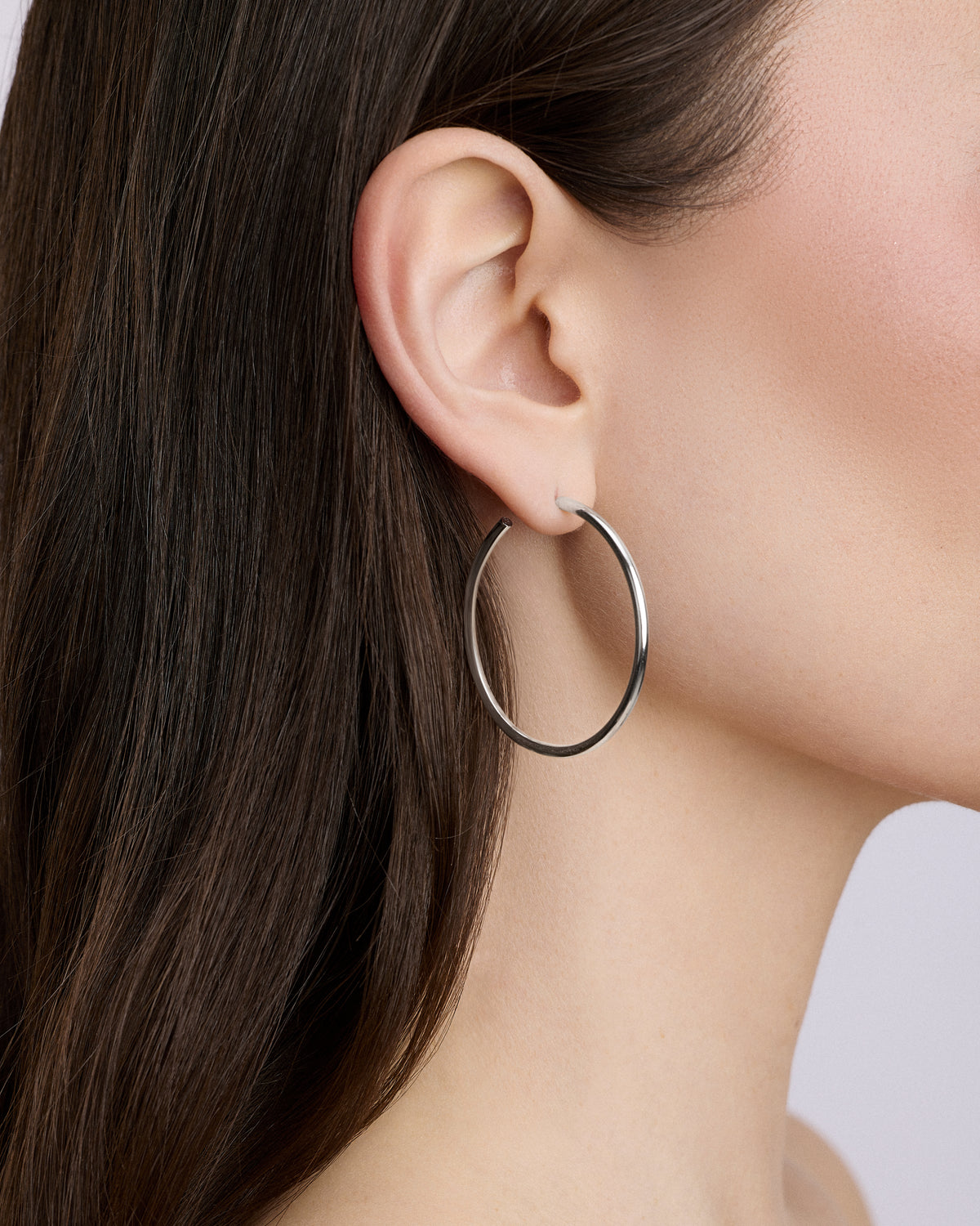 Silver hoop earring worn by a person with dark hair.