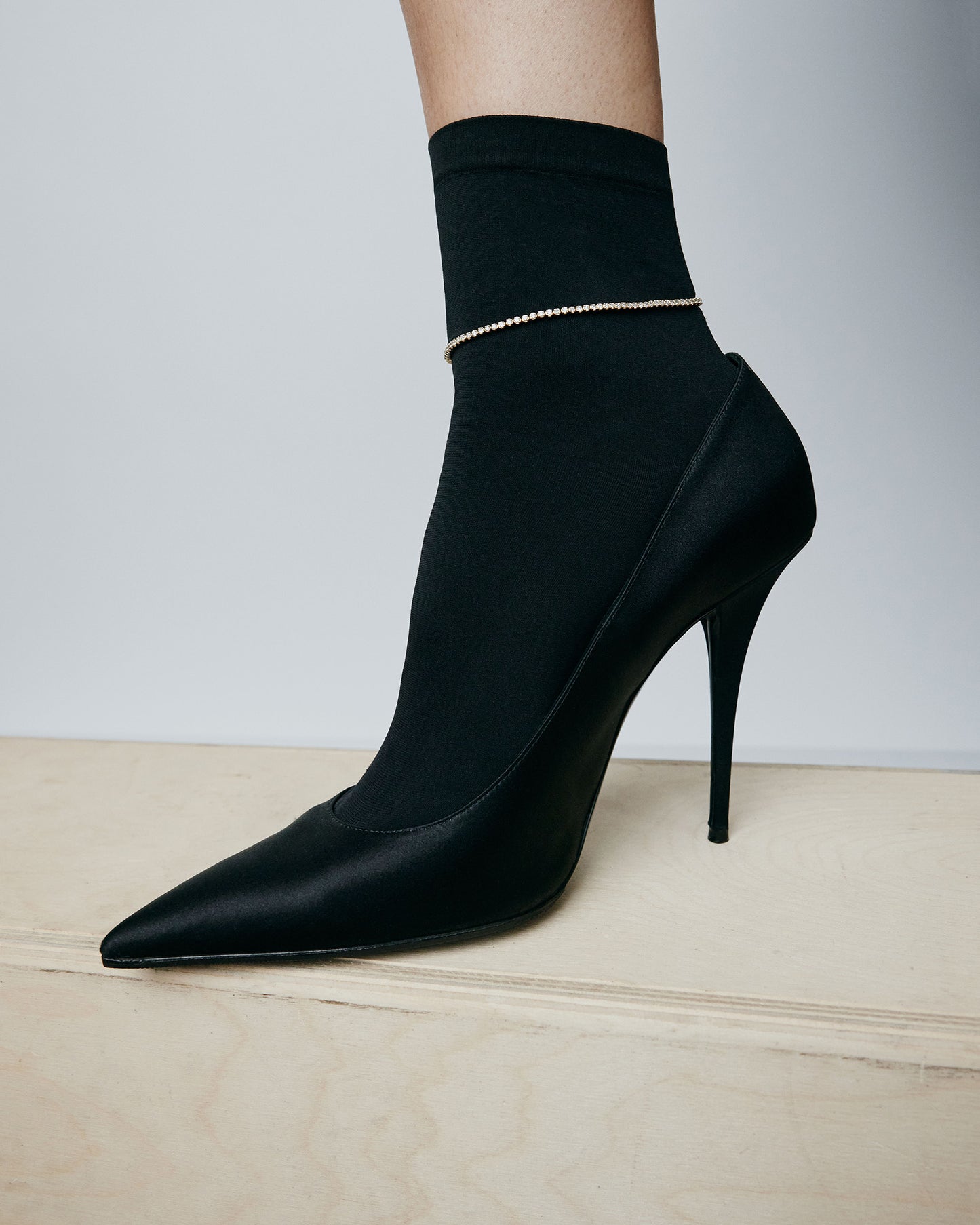 Image of a foot with a black heel and opaque black sock with diamond anklet layered over the top. 