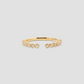 A delicate gold open ring featuring a row of small bezel-set round clear stones on the front, photographed against a solid light gray background.