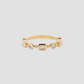 A gold band ring featuring a row of clear baguette and round-cut gemstones, displayed on a neutral light gray background.