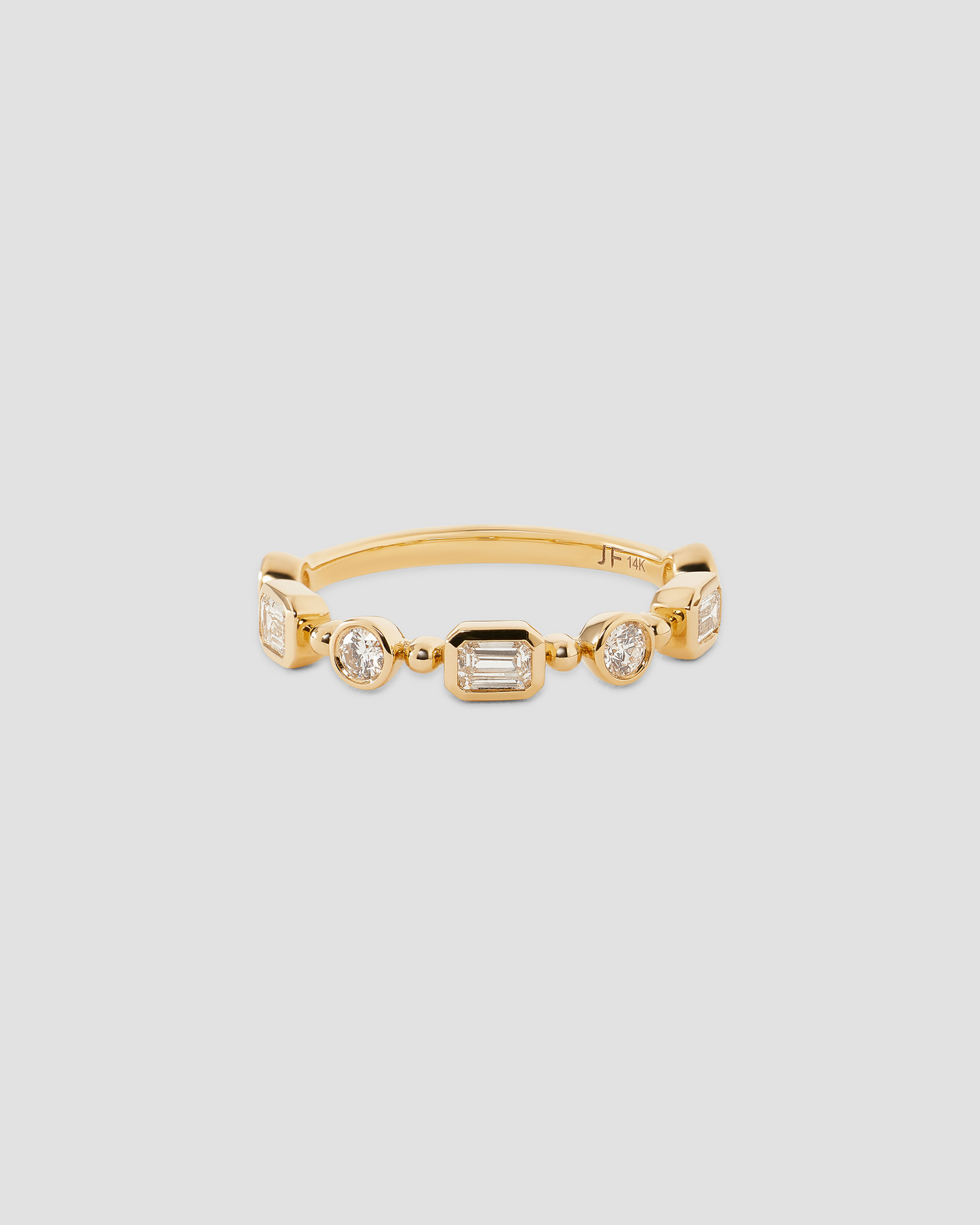 A gold band ring featuring a row of clear baguette and round-cut gemstones, displayed on a neutral light gray background.