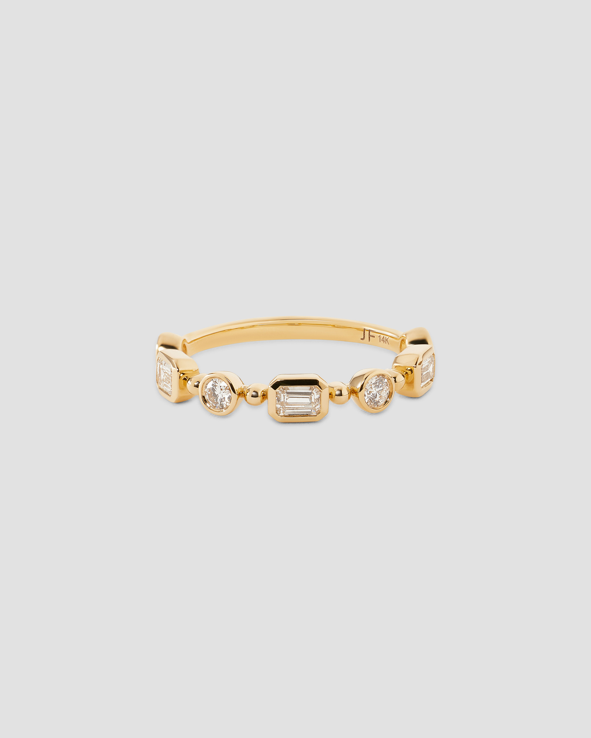 A gold band ring featuring a row of clear baguette and round-cut gemstones, displayed on a neutral light gray background.