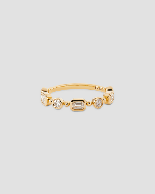 A gold band ring featuring a row of clear baguette and round-cut gemstones, displayed on a neutral light gray background.