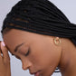 Woman with braided hair wearing gold hoop earrings against a gray background
