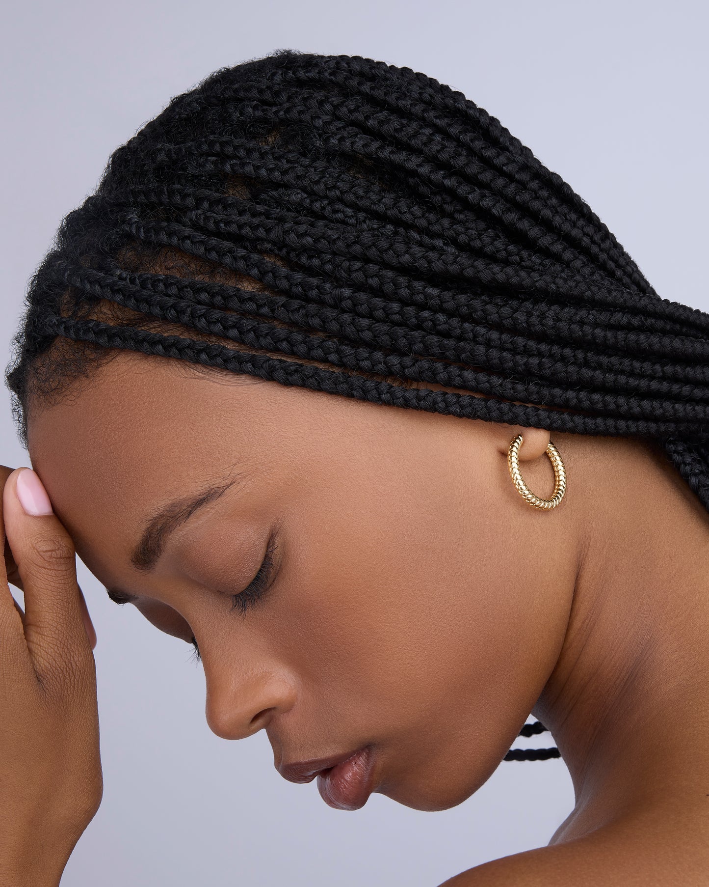 Woman with braided hair wearing gold hoop earrings against a gray background