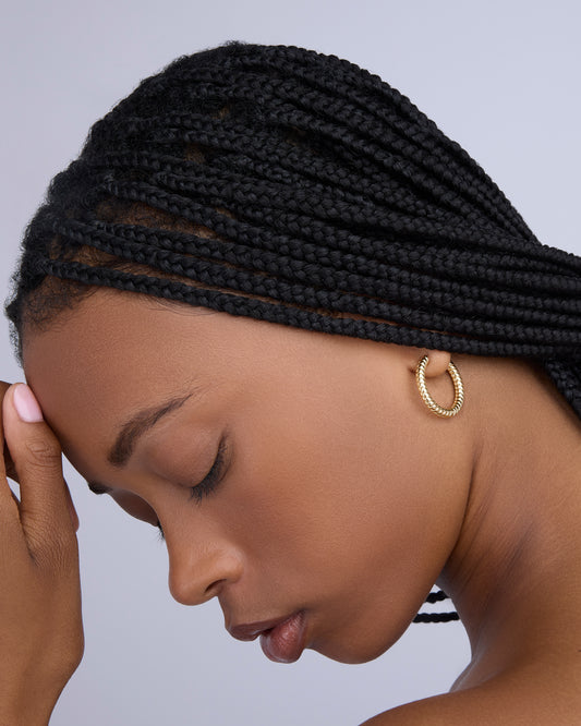 Woman with braided hair wearing gold hoop earrings against a gray background